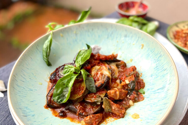 Ein Teller mit Auberginen-Auflauf, garniert mit frischen Basilikumblättern.