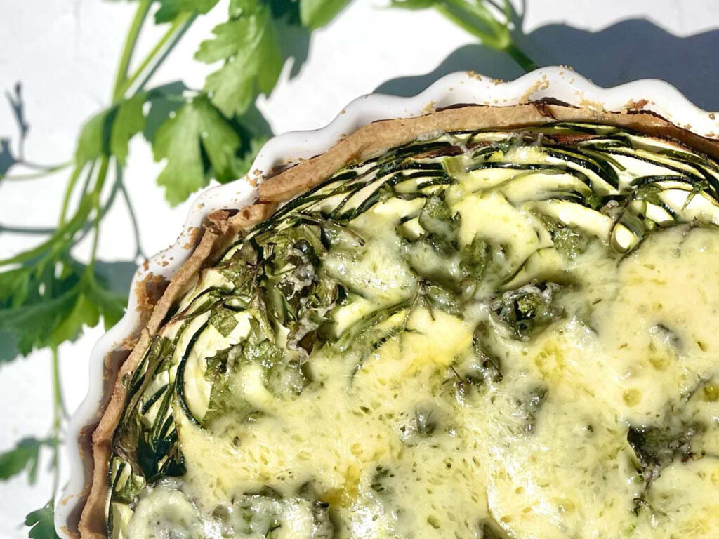 Nahaufnahme einer Zucchini-Quiche in klassischer Quicheform mit goldbrauner Kruste