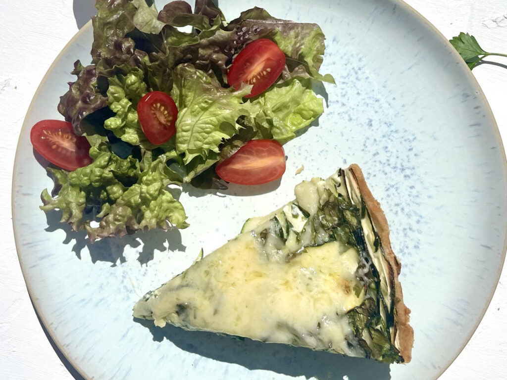 Ein Stück Zucchini-Petersilie-Quiche auf einem Teller mit Salat und Kirschtomaten