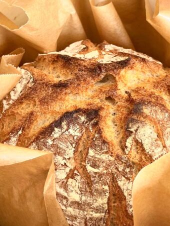 Brot selber backen, Ein frisch gebackenes Brot in einem gusseisernen Topf, umgeben von Backpapier.