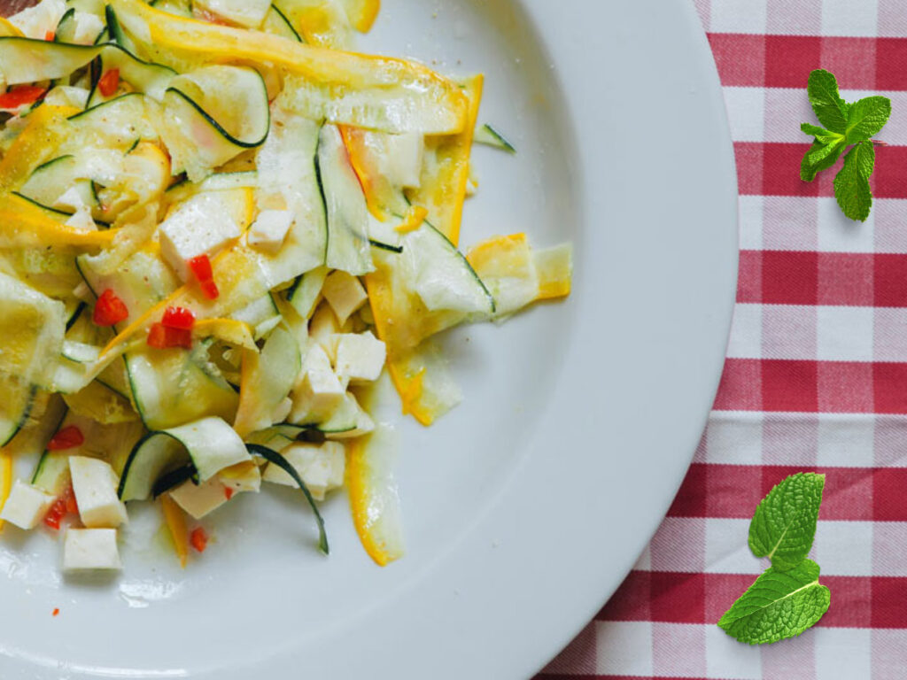 Zucchinisalat mit gelben und grünen Zucchinistreifen, Mozzarella und Chili auf einem weißen Teller