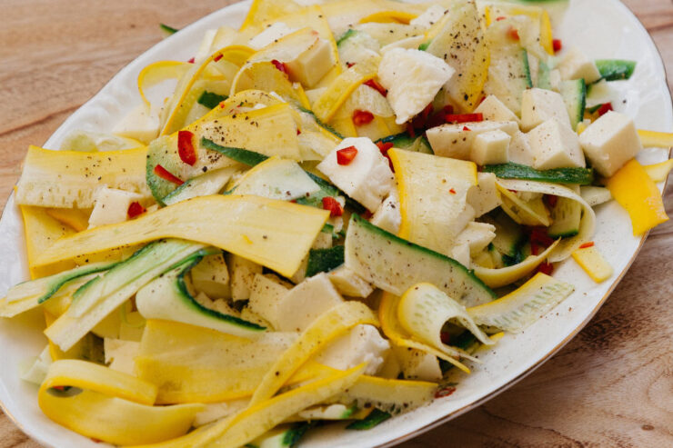 Frischer Zucchinisalat mit gelben und grünen Zucchinistreifen, Mozzarella und Chili