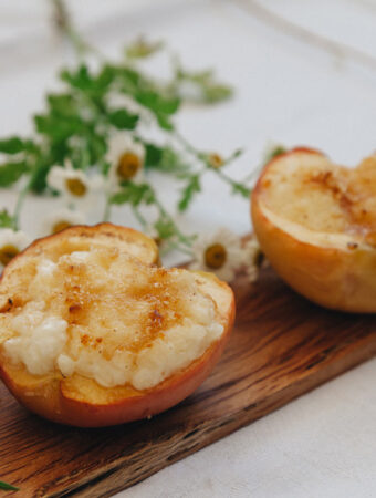 Nahaufnahme einer gebackenen Apfelhälfte, gefüllt, auf einem Holzbrett mit Blumen dekoriert.