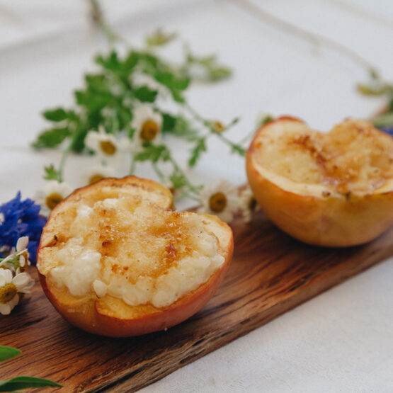 Nahaufnahme einer gebackenen Apfelhälfte, gefüllt, auf einem Holzbrett mit Blumen dekoriert.