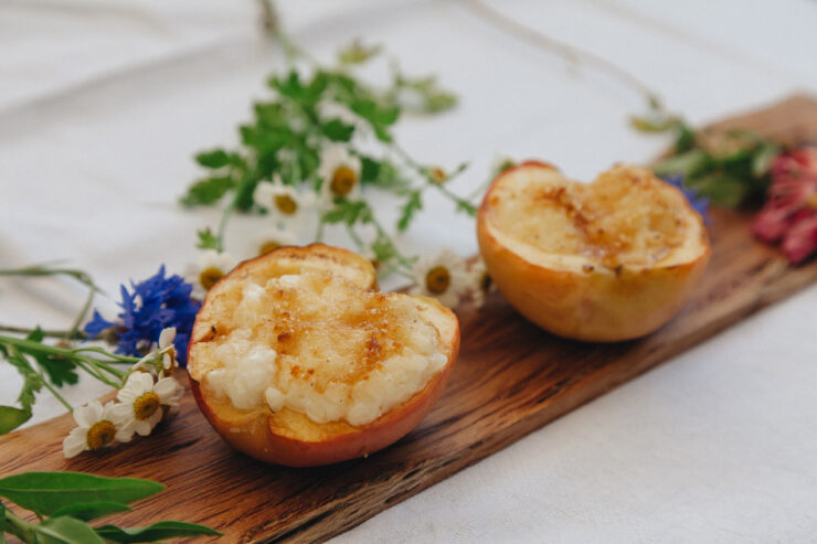 Nahaufnahme einer gebackenen Apfelhälfte, gefüllt, auf einem Holzbrett mit Blumen dekoriert.