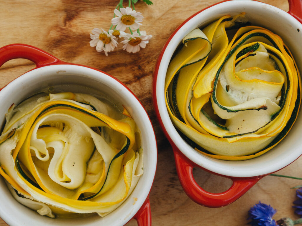 Zucchini und gelbe Zucchini als feine Streifen in einer roten Ofenform, ideal für eine gesunde und schnelle Mahlzeit