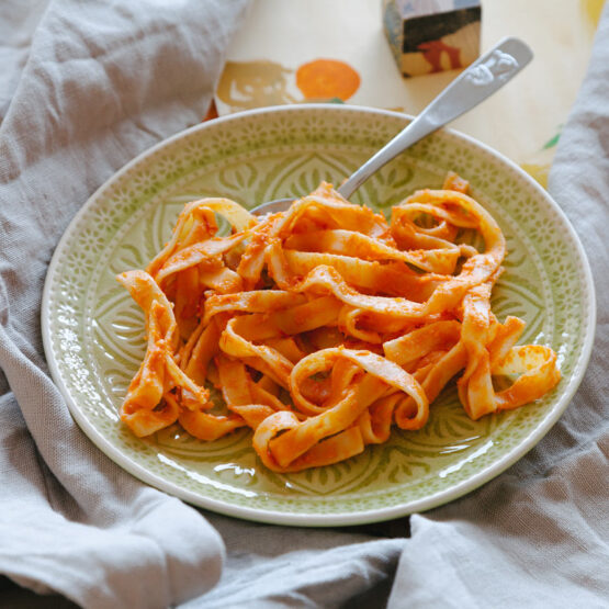 Pasta auf einem grünen Teller, im Hintergrund bunte Holzklötze und ein Leinentuch.