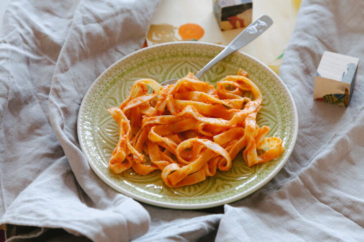 Pasta auf einem grünen Teller, im Hintergrund bunte Holzklötze und ein Leinentuch.