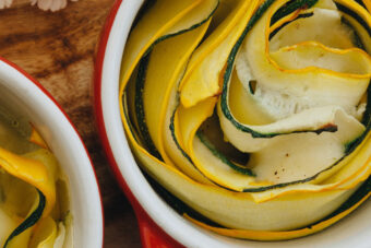 Grüne und gelbe Sommerkürbisse in Rosettenform in einer kleinen roten Backform, perfekt als vegetarische Beilage