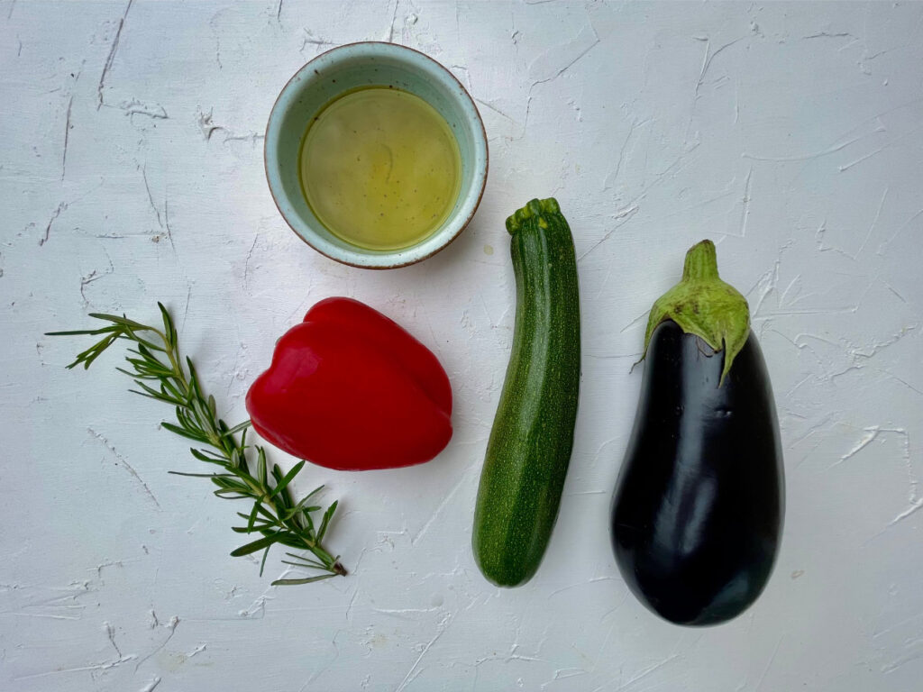 utaten für Caponata Rezept: Aubergine, Zucchini, rote Paprika, Olivenöl und Rosmarin auf hellem Untergrund
