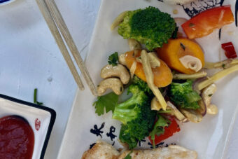 Längliche Platte mit Gemüse, gebratenem Huhn, Reisberg und rotem Dip, daneben Essstäbchen.