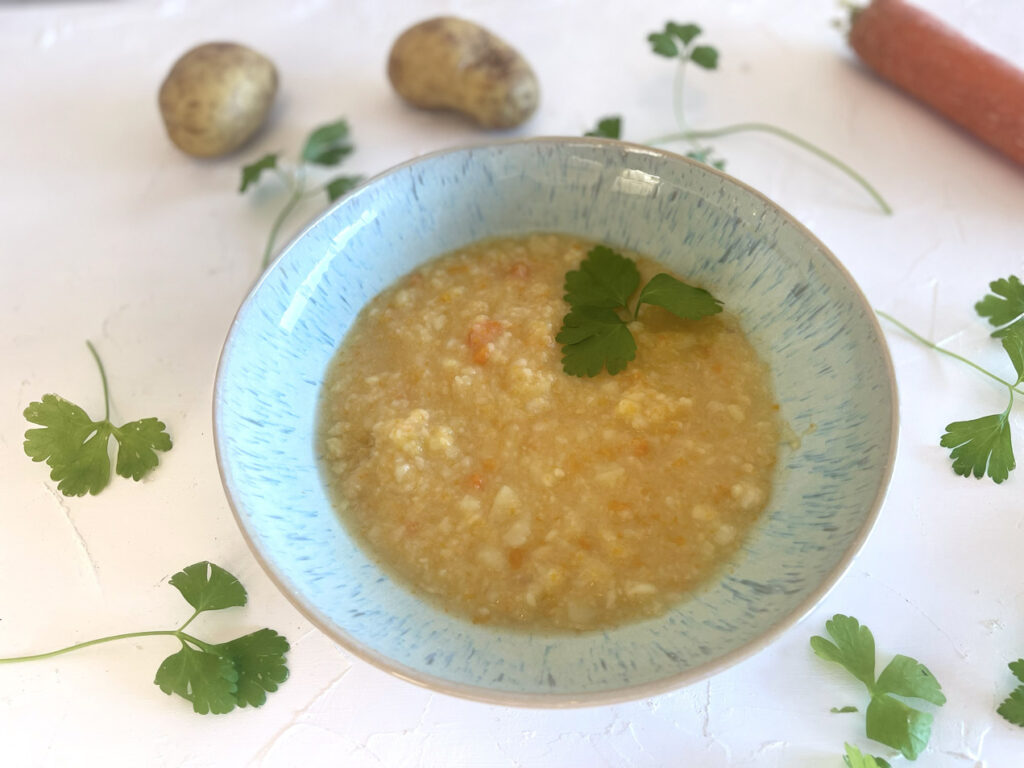 Cremige Kartoffelsuppe mit Möhren in einer hellblauen Schüssel, garniert mit frischer Petersilie auf hellem Hintergrund.