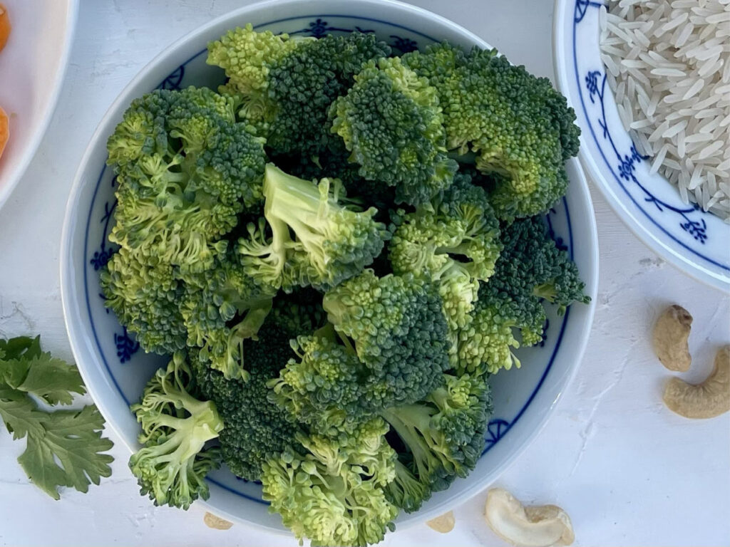 Schüssel mit frischem Brokkoli daneben Reis und Cashews.
