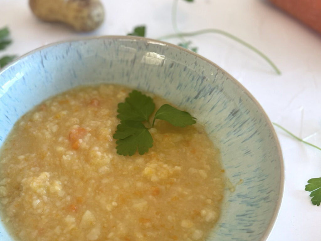 Rustikale Kartoffelsuppe wie bei Oma in einer hellblauen Schale, umgeben von frischer Petersilie und Kartoffeln.