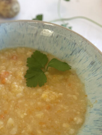 Rustikale Kartoffelsuppe wie bei Oma in einer hellblauen Schale, umgeben von frischer Petersilie und Kartoffeln.