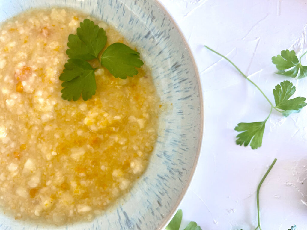 Klassische Kartoffelsuppe mit Stückchen in blauer Schüssel, dekoriert mit Petersilie, daneben rohe Kartoffeln und Möhren.